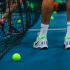 persona jugando tenis con zapatos para jugar tenis marca Nike blancos con verde parado junto a malla de tenis