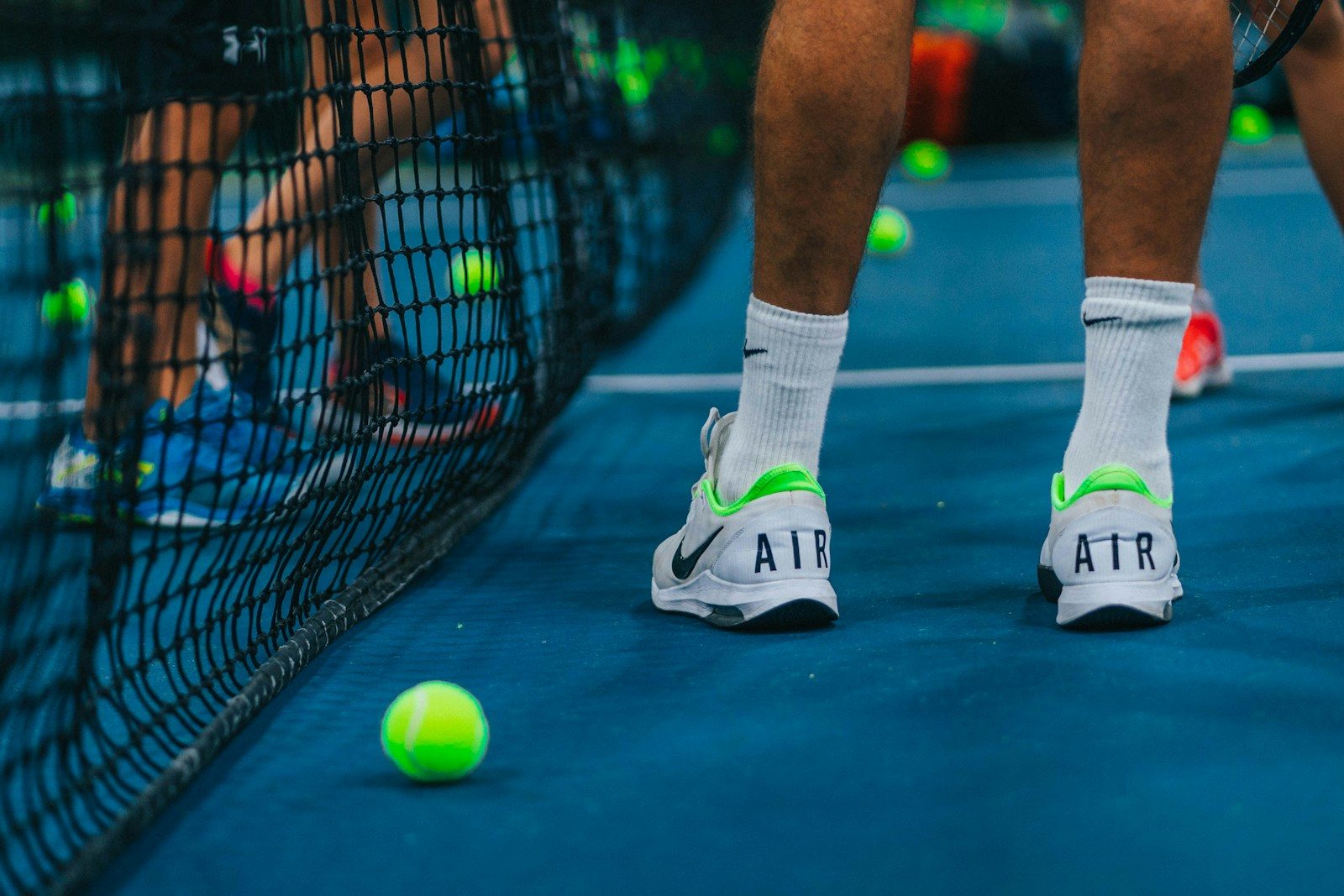 persona jugando tenis con zapatos para jugar tenis marca Nike blancos con verde parado junto a malla de tenis