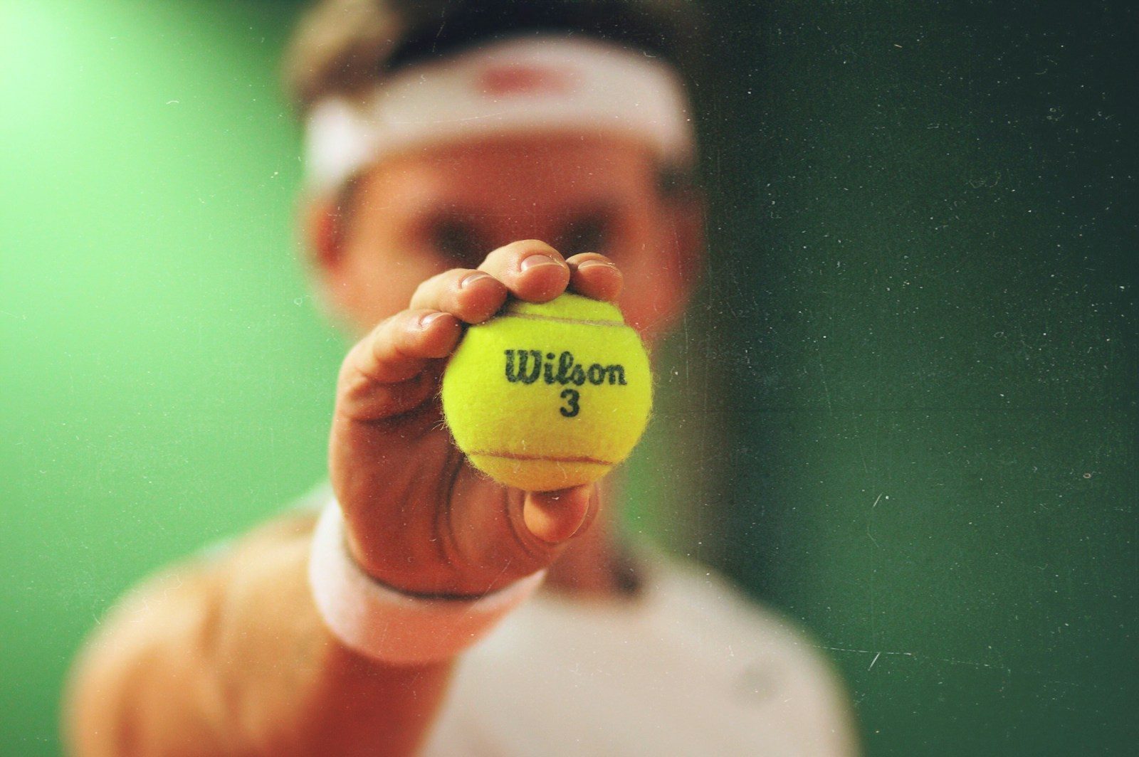 Jugador de tenis sosteniendo pelota de tenis marca Wilson mostrándola hacia la cámara.